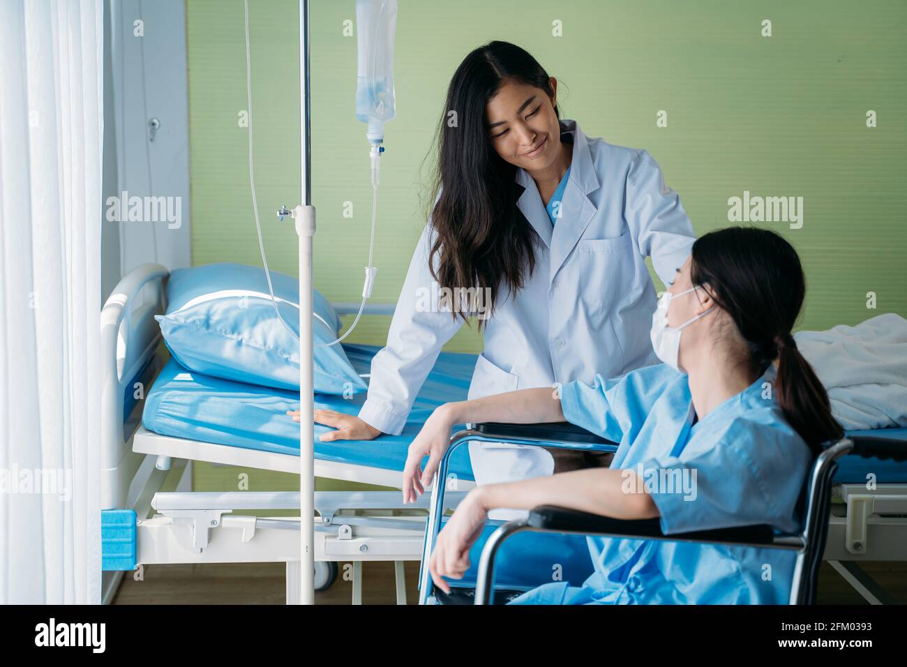 Lächelnd junge asiatische Ärztin, die Routineuntersuchungen macht und spricht Und beruhigende depressive Patienten, die auf dem Rollstuhl auf der Krankenhausstation sitzen Stockfoto