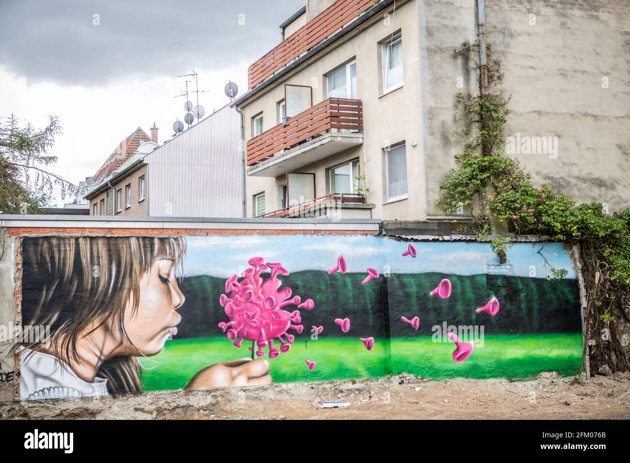 Ein Graffiti an einer alten Mauer zeigt ein Mädchen, welches wie bei einer Pusteblume ein Coronavirus anpustet, welches dann auseinander fliegt. Ein s Stockfoto