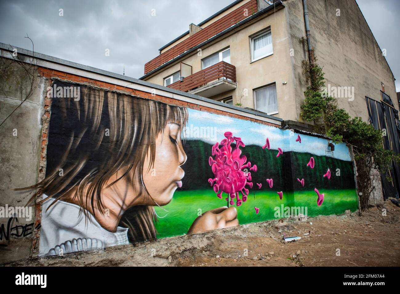 Ein Graffiti an einer alten Mauer zeigt ein Mädchen, welches wie bei einer Pusteblume ein Coronavirus anpustet, welches dann auseinander fliegt. Ein s Stockfoto