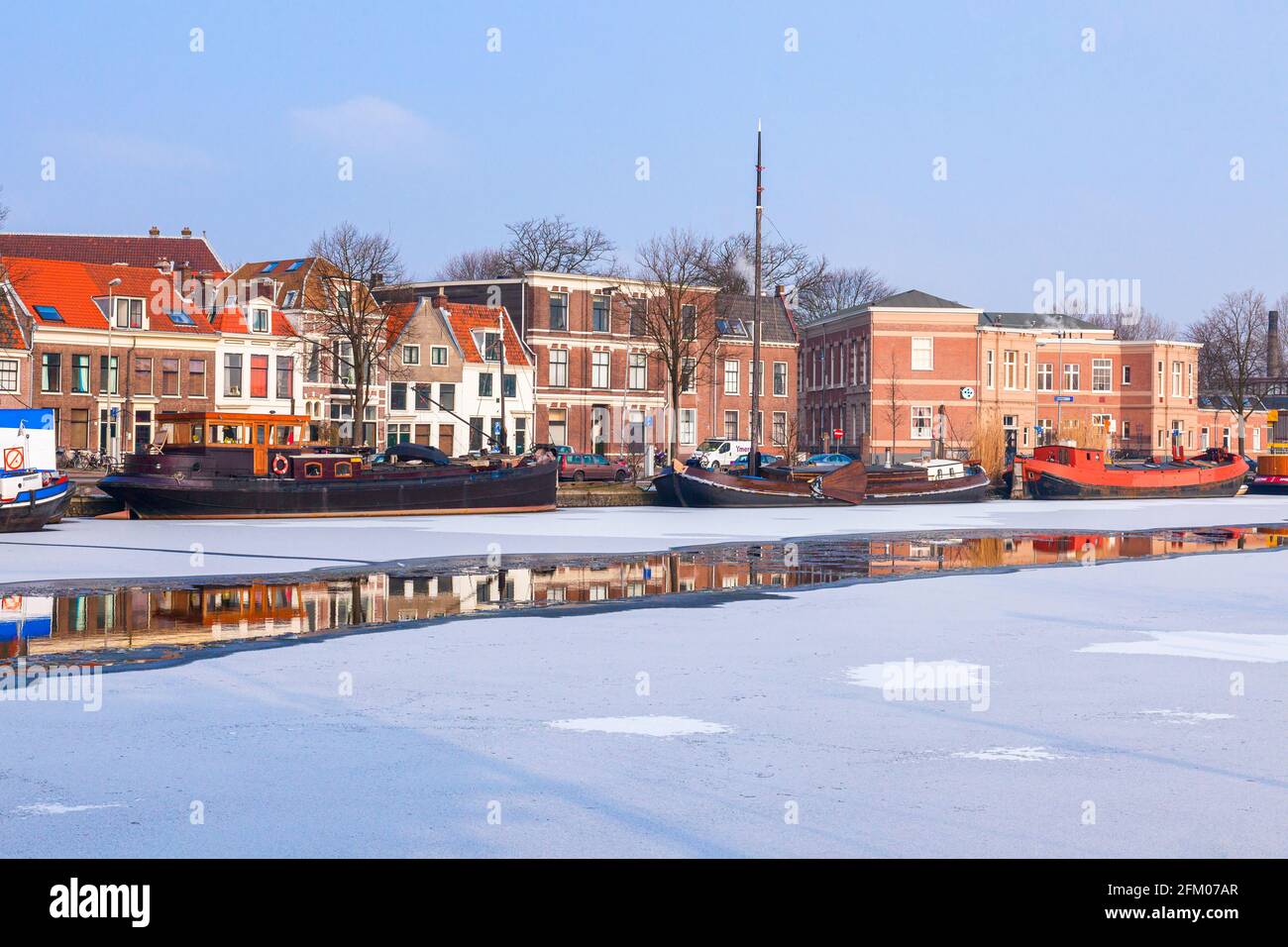 Traditionelle Häuser und Boote, die im gefrorenen Kanal des Flusses Spaarne, Haarlem, Amsterdam, Nordholland, Niederlande, festgemacht sind Stockfoto