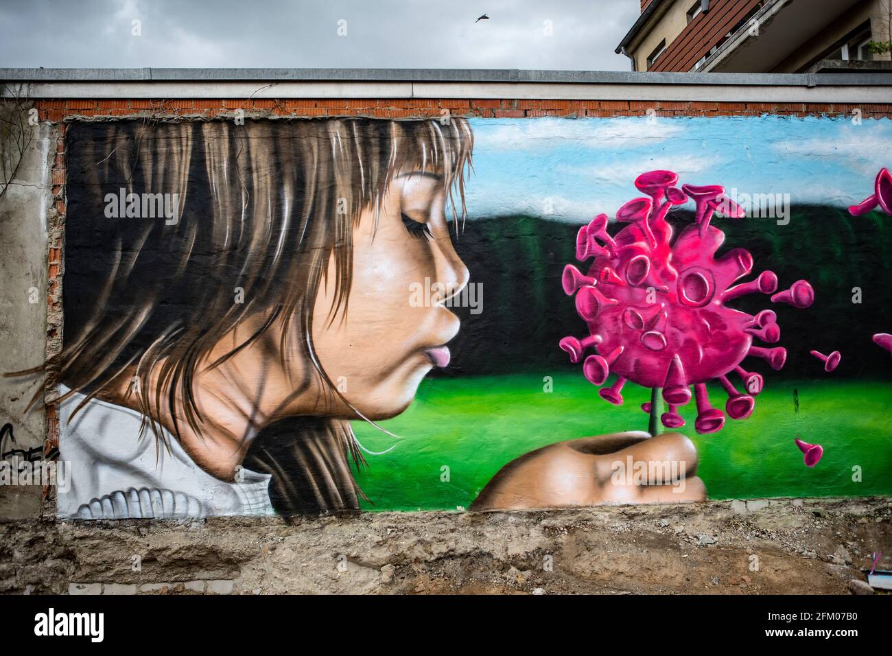 Ein Graffiti an einer alten Mauer zeigt ein Mädchen, welches wie bei einer Pusteblume ein Coronavirus anpustet, welches dann auseinander fliegt. Ein s Stockfoto