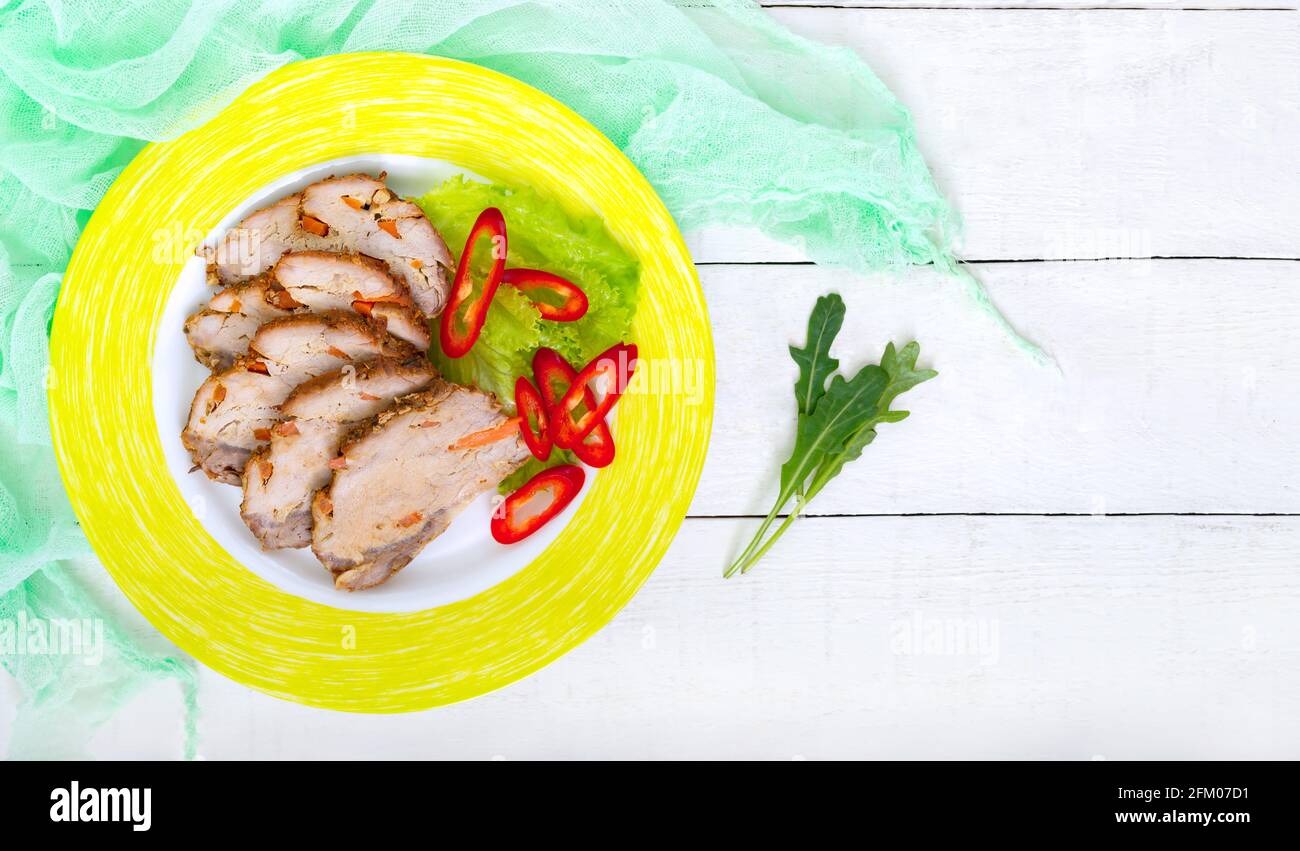 Gebackenes Schweinefleisch mit Karotten, in Scheiben geschnitten auf einem Teller mit frischem Gemüse auf dem weißen Holzhintergrund. Draufsicht, flach liegend. Speicherplatz kopieren. Stockfoto