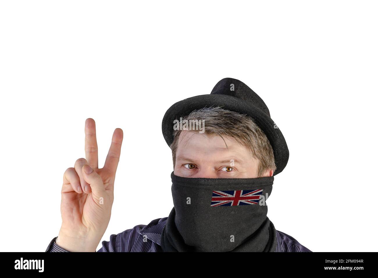 Ein erwachsener Mann in einem schwarzen Hut mit kleinen Feldern und einem Schal über seinem Gesicht zeigt eine Siegesgeste. Schal mit Flagge von Großbritannien. Ein nicht erkennbarer Pers Stockfoto