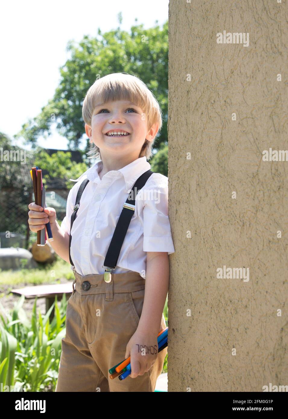 Fröhlich niedlichen Jungen 5-6 Jahre alt ist die Vorbereitung für die Schule. Steht an einem sonnigen Tag im Freien in einem weißen Hemd und hält bunte Filzstifte in seinem han Stockfoto