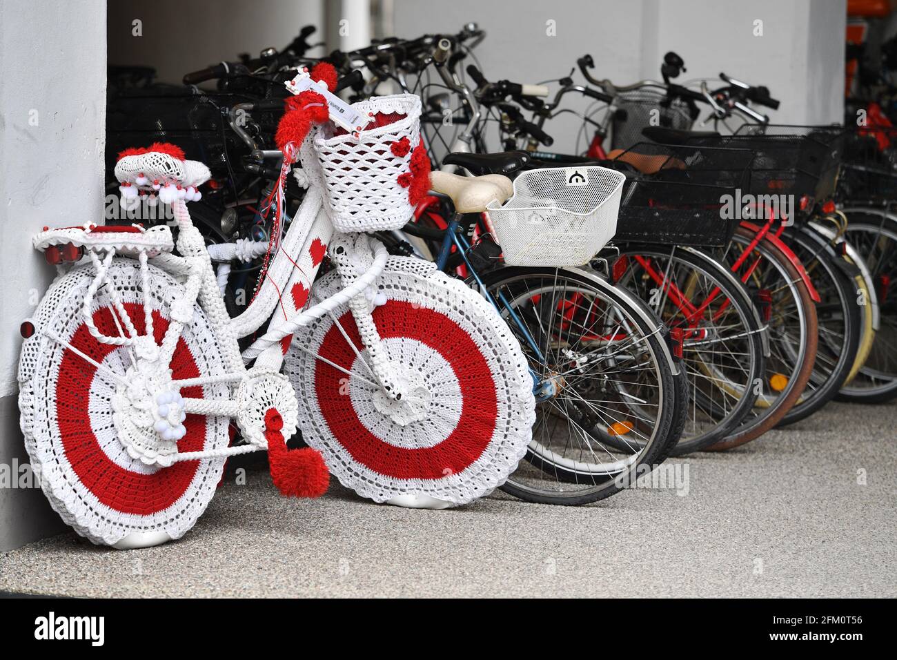 München, Deutschland. Mai 2021. Auffälliges Deko-Fahrrad im Haekel-Kleid  befindet sich auf dem Marienplatz in München. Neben geparkten Fahrrädern  sticht ein ganz besonderes Fahrrad hervor - es ist in weißen, roten Stoff,  Wolle