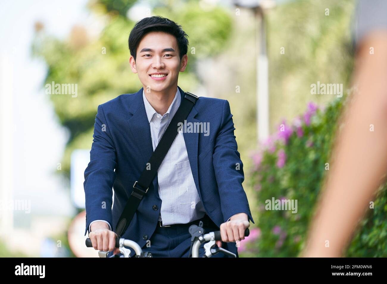 Junger asiatischer Geschäftsmann, der mit dem Fahrrad zur oder von der Arbeit fährt, glücklich und lächelnd Stockfoto