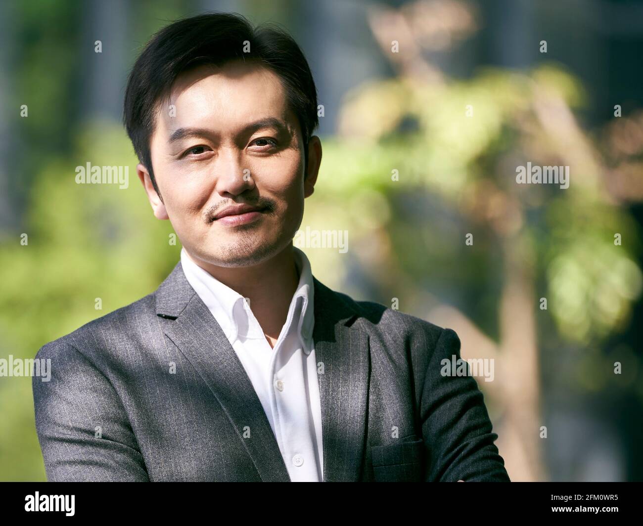 Porträt eines erfolgreichen asiatischen Geschäftsmannes im Freien, der lächelnd auf die Kamera schaut Stockfoto