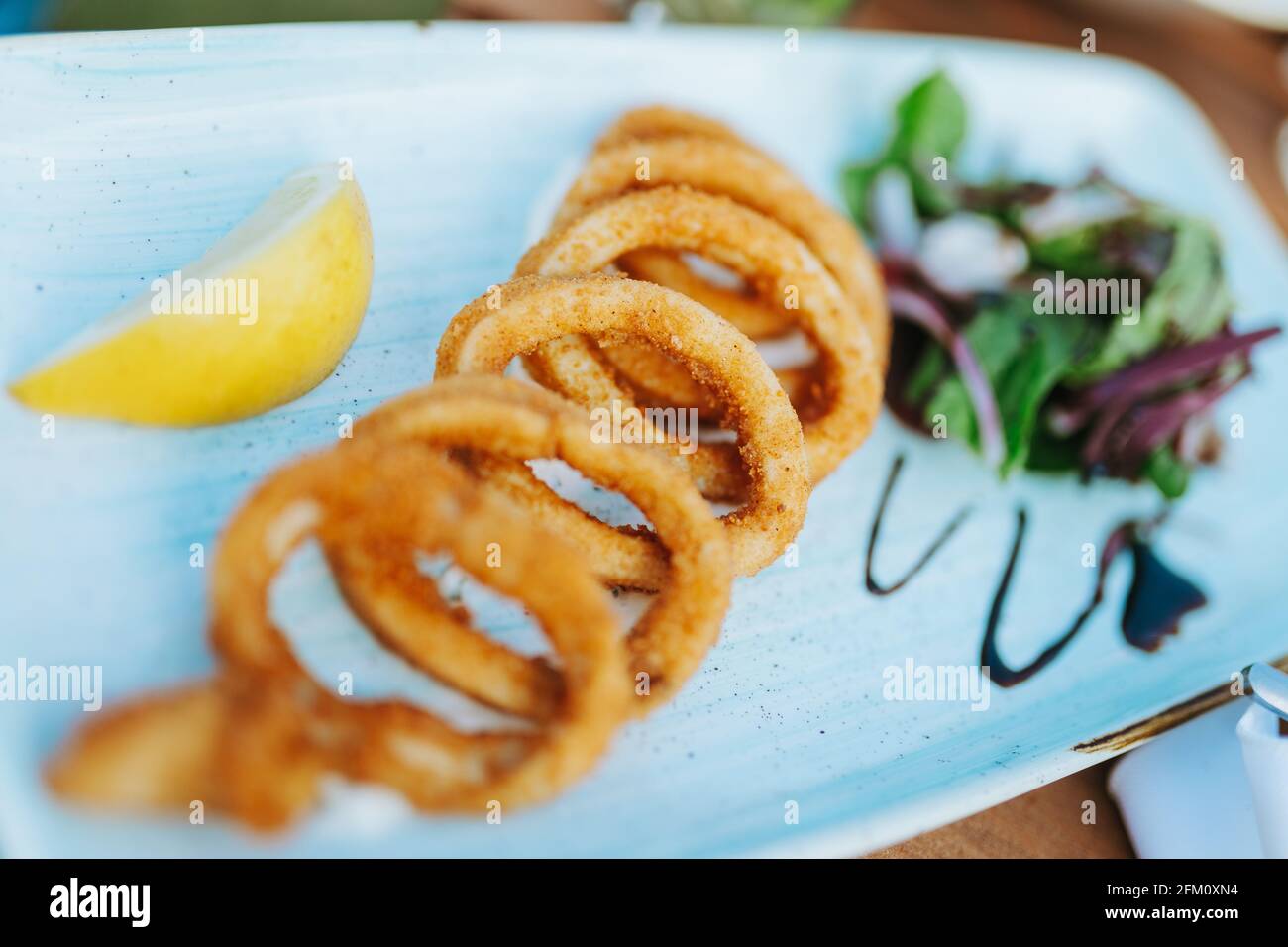 Frittierte Tintenfische oder Tintenfisch Calamari Ringe mit Salat und Zitrone auf einem weißen Teller Stockfoto