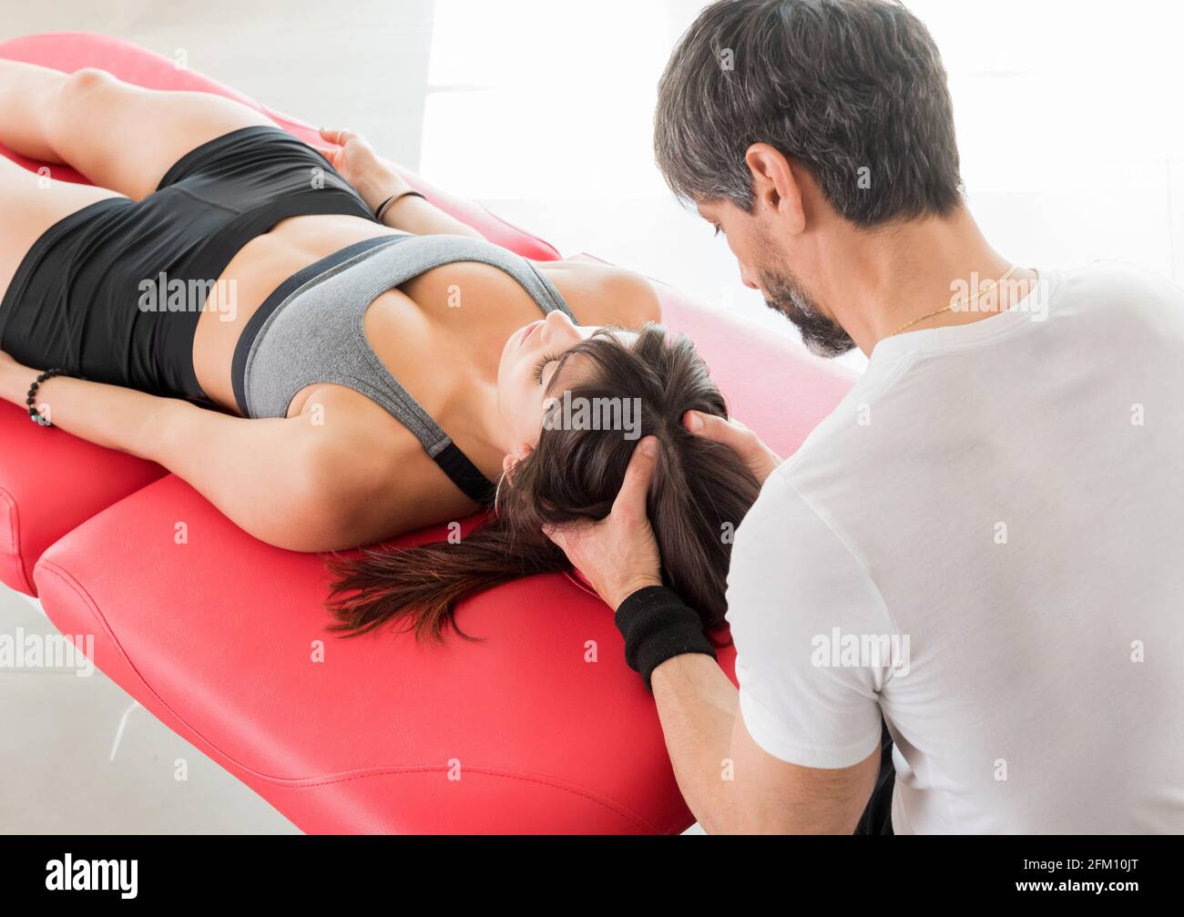 Junger männlicher Osteopath, der eine kraniosakrale Massage an einem Weibchen macht Der Patient massiert und tapiert sanft den Schädel und die Rückenmarksflüssigkeit Mit den Händen Stockfoto