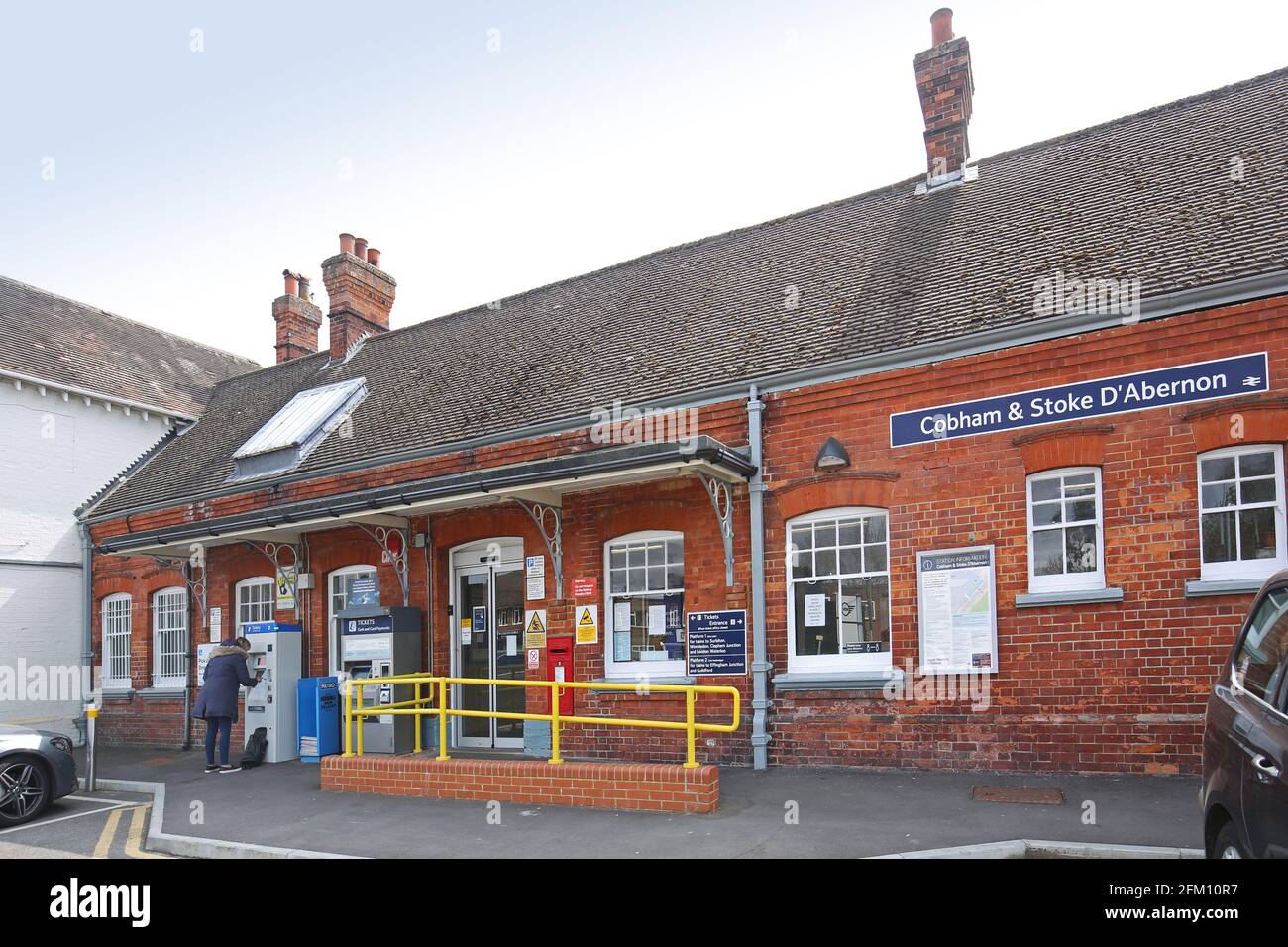 Eintritt zu Cobham und Stoke D'Abernon Station, Surrey. Typischer viktorianischer Bahnhof in den Vororten von London, Großbritannien. Zeigt den Passagier, der den Ticketautomaten benutzt. Stockfoto