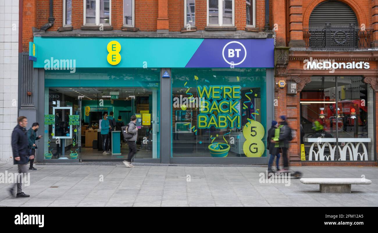 Elektroroller Fahrer auf Oxford Street Bürgersteig passiert Fußgänger mit Geschwindigkeit vor BT und EE Handy-Shop, 4. Mai 2021 Stockfoto