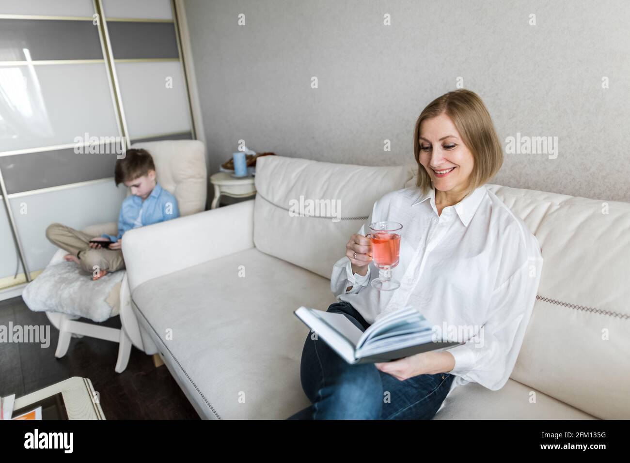 Die Frau sitzt auf der Couch und hält ein Buch in der Hand und trinkt Tee. Stockfoto