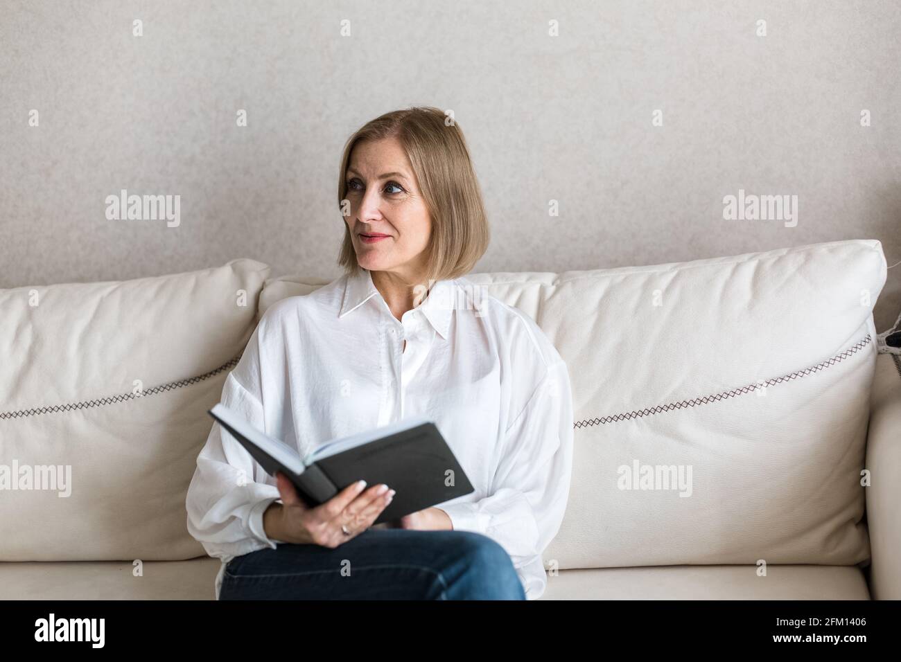 Die Frau sitzt auf der Couch und hält ein Buch in der Hand. Stockfoto