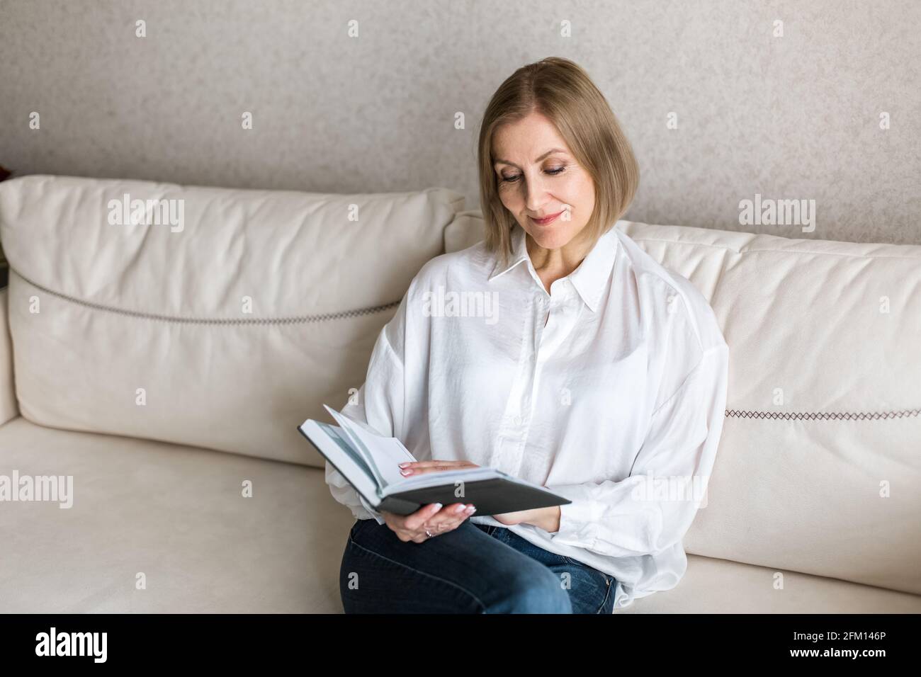 Die Frau sitzt auf der Couch und hält ein Buch in der Hand. Stockfoto