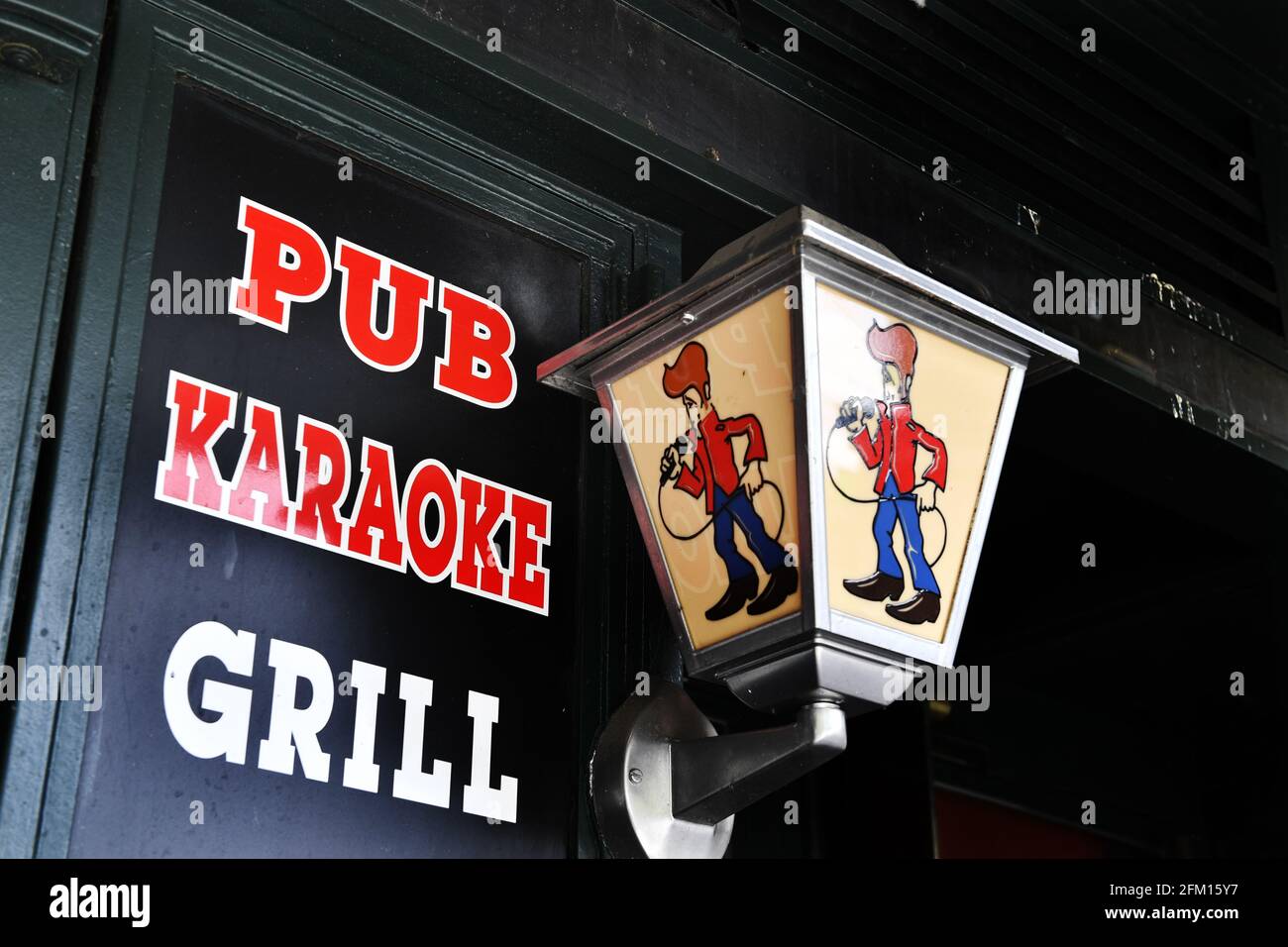ein Pub-Schild mit den Worten "PUB KARAOKE GRILL" neben einer dekorativen Wandlaterne mit einer Cartoonfigur, die ein Mikrofon hält, gelegen in Paris, Stockfoto