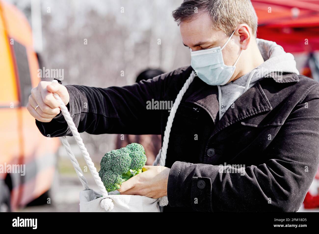 Maskierter Mann auf dem lokalen Markt, der Brokkoli-Kohl in der Zeit der Pandemie kauft. Covid Pandemic Shopping-Konzept. Hochwertige Fotos Stockfoto