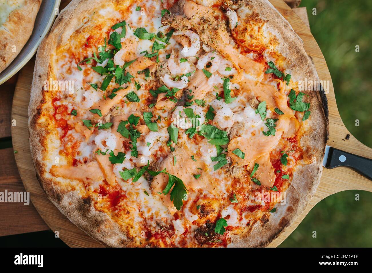 Pescatore Pizza mit Lachs Thunfisch Garnelen Mozzarella auf einem hölzernen Rundes Tablett Stockfoto