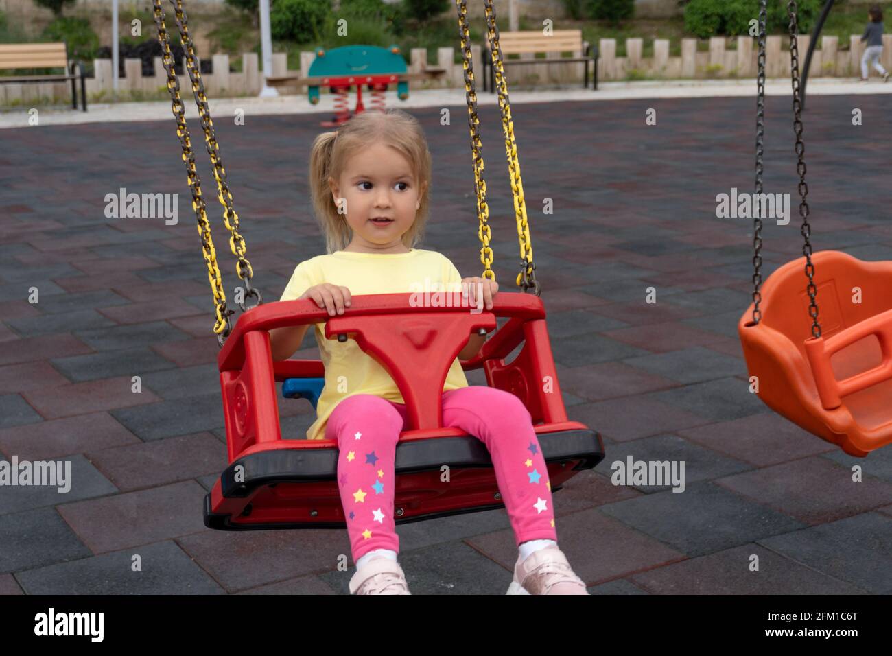 Niedliches kaukasisches Kind schwingt auf Schaukel, mit interessierter und überraschendem Ausdruck. Stockfoto