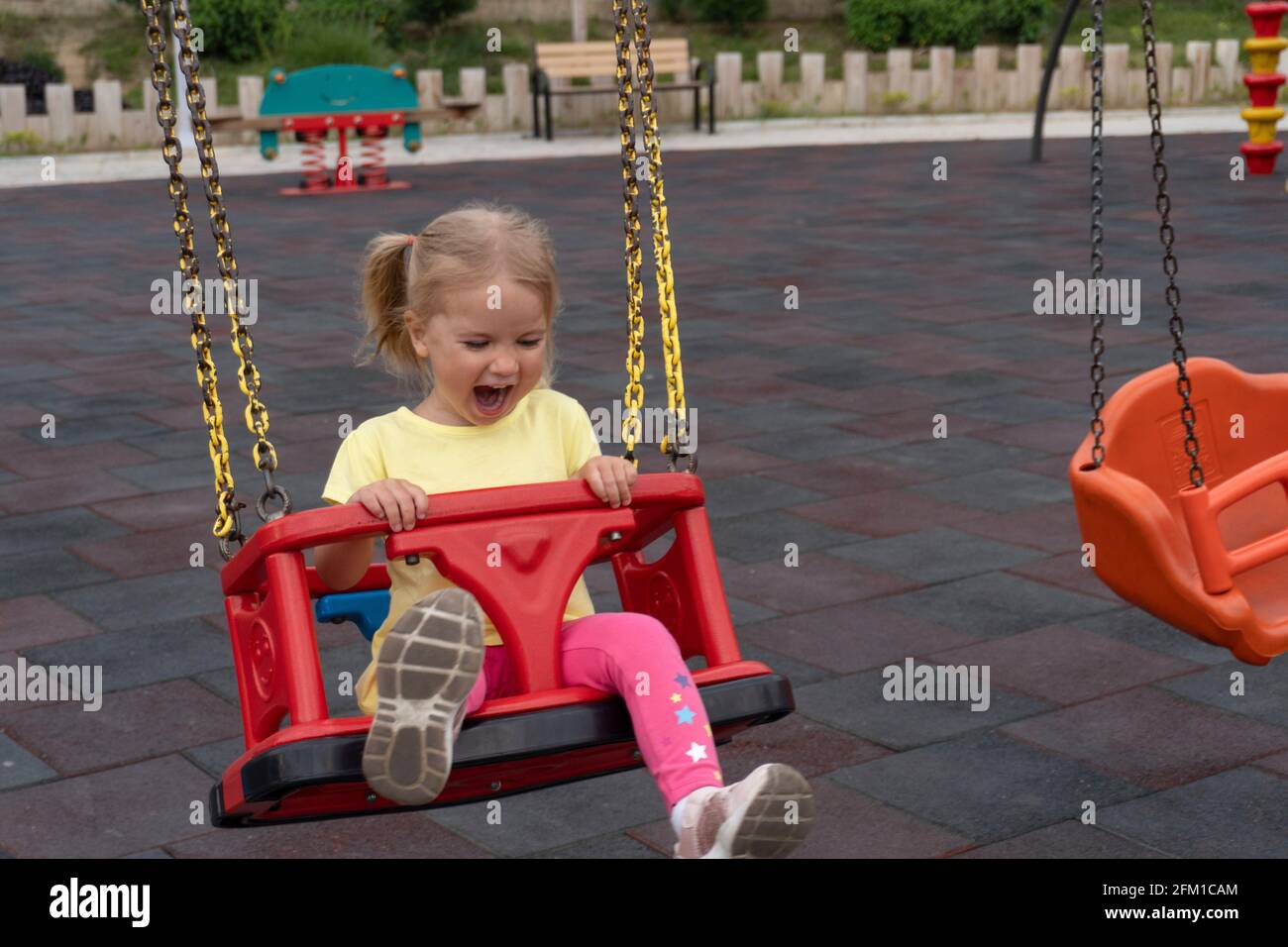 Niedliches kaukasisches Kind schwingt auf Schaukel, lacht und weint mit fröhlichem Ausdruck Stockfoto