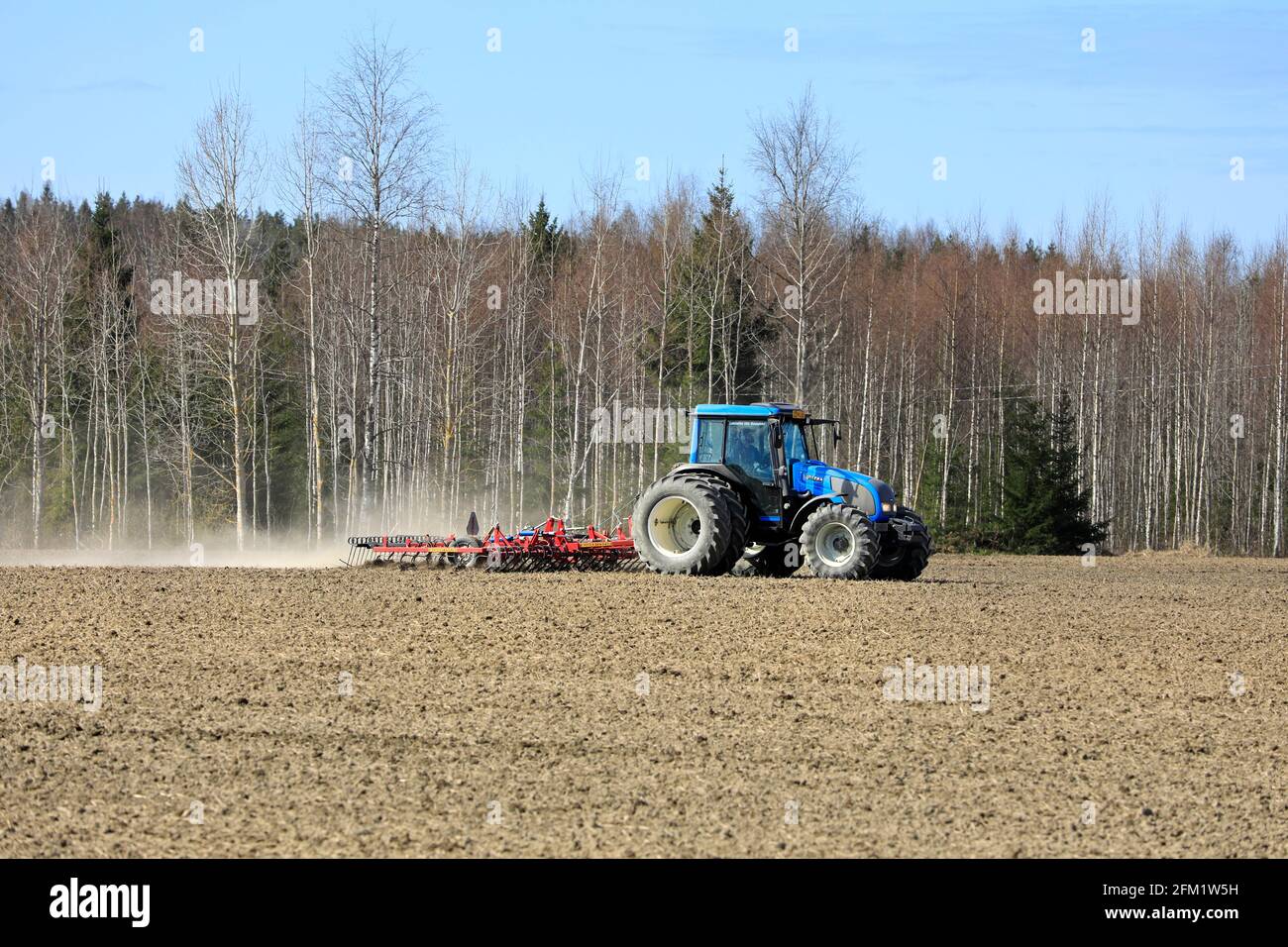 Landwirt kultiviert Feld mit blauen Valtra Traktor und Potila SKH 540 Egge an einem schönen Frühlingsmorgen. Salo, Finnland. 2.Mai 2021. Stockfoto