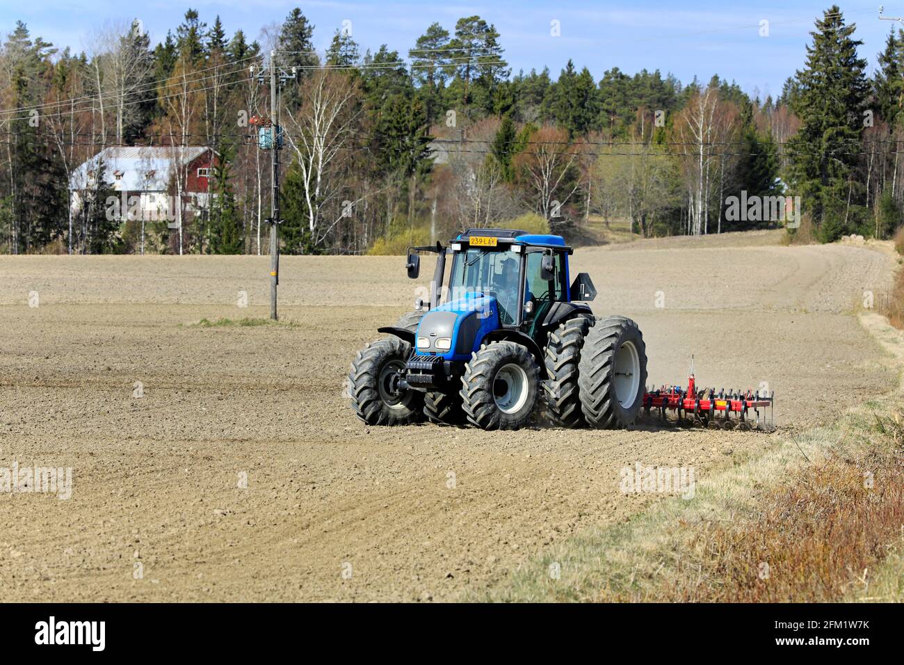 Landwirt kultiviert Feld mit blauen Valtra Traktor und Potila SKH 540 Egge an einem schönen Frühlingsmorgen. Salo, Finnland. 2.Mai 2021. Stockfoto