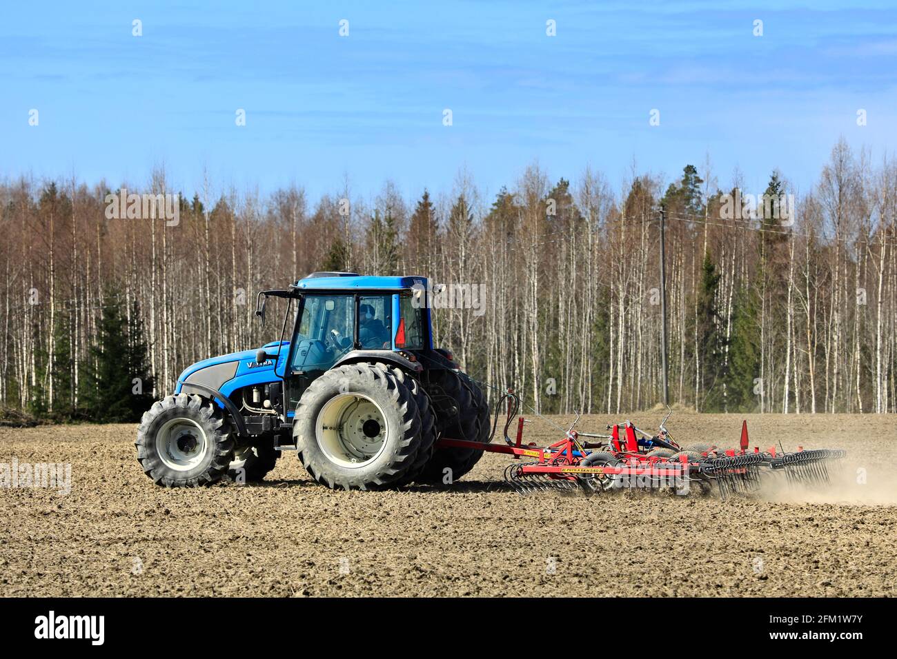 Landwirt kultiviert Feld mit blauen Valtra Traktor und Potila SKH 540 Egge an einem schönen Frühlingsmorgen. Salo, Finnland. 2.Mai 2021. Stockfoto