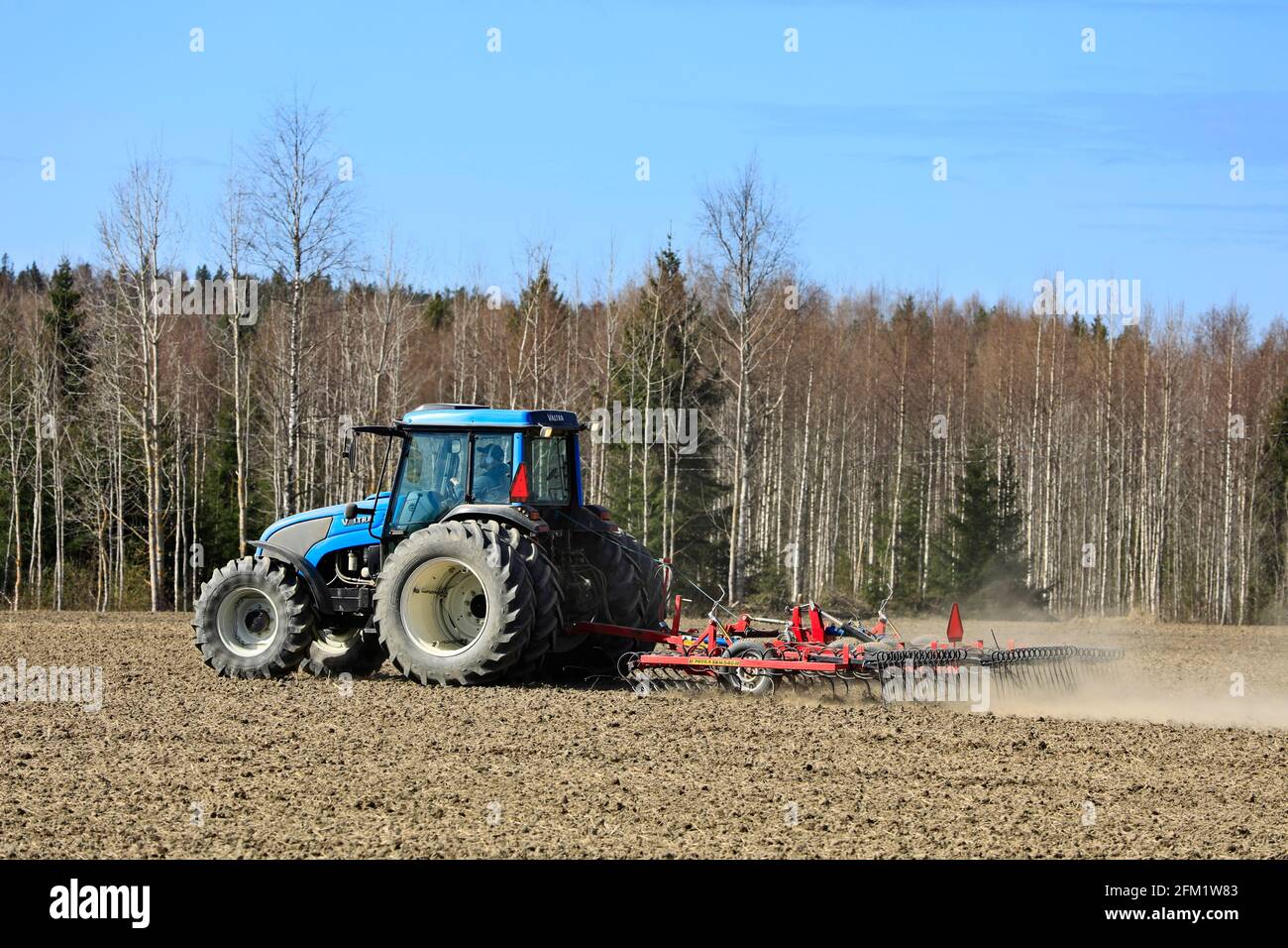Landwirt kultiviert Feld mit blauen Valtra Traktor und Potila SKH 540 Egge an einem schönen Frühlingsmorgen. Salo, Finnland. 2.Mai 2021. Stockfoto