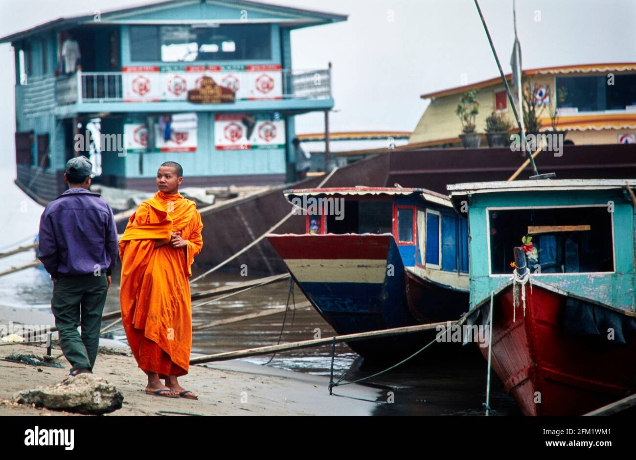 Ein junger buddhistischer Mönch wartet am Strand des Mekong in Luang Prabang auf die Abfahrt eines Bootes. 12/1996 - Christoph Keller Stockfoto