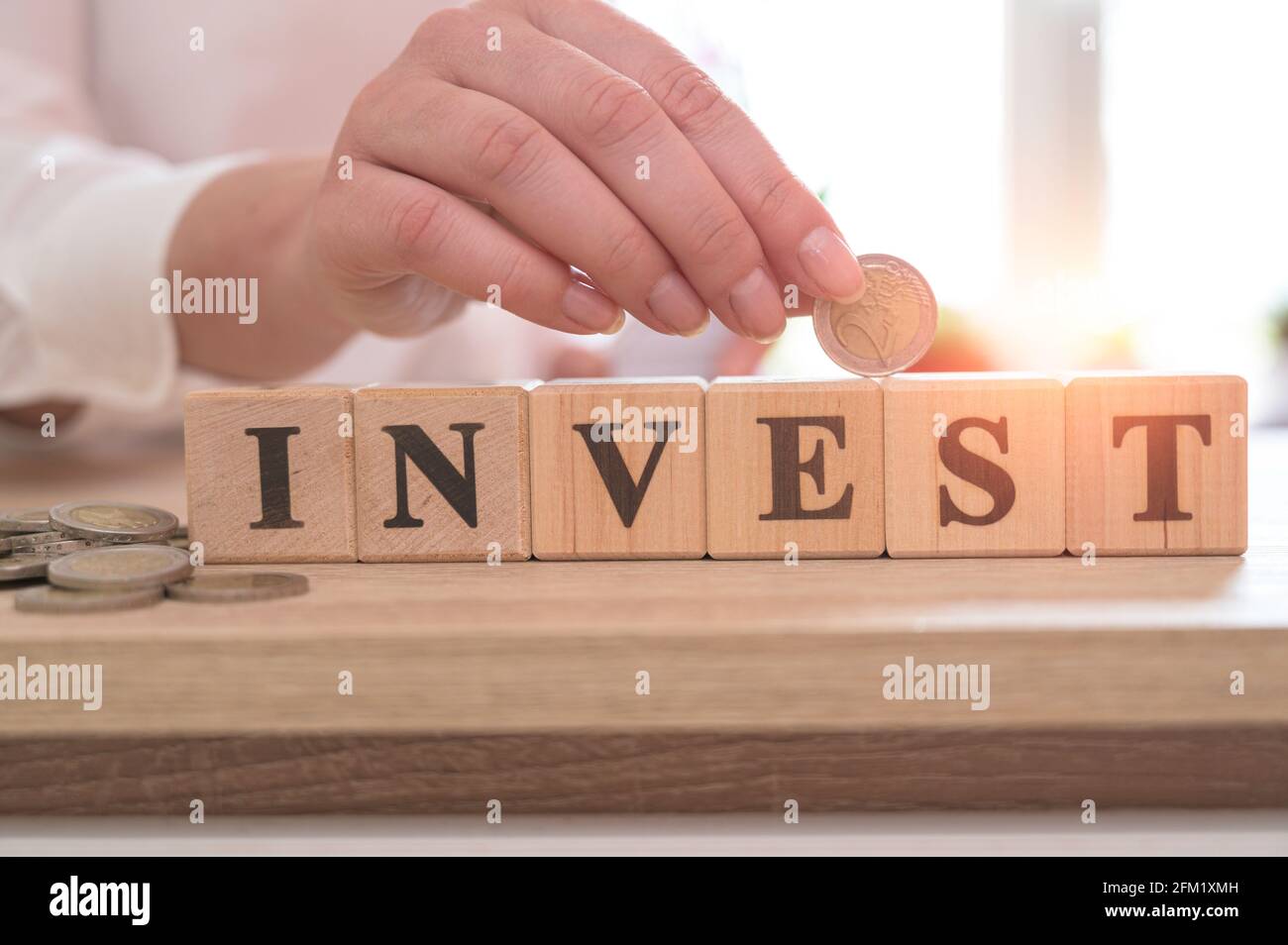 Wort INVESTIEREN auf Holzwürfel und Hand halten Euro-Münze. Investitionskonzept. Stockfoto