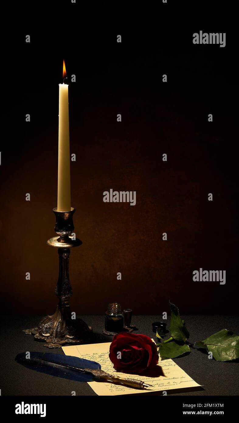 Eine Kerze in Kerzenständer, roter Rose, Brief und Federstift auf dunklem Grund wird durch das Kerzenlicht aufgehellt. Stockfoto
