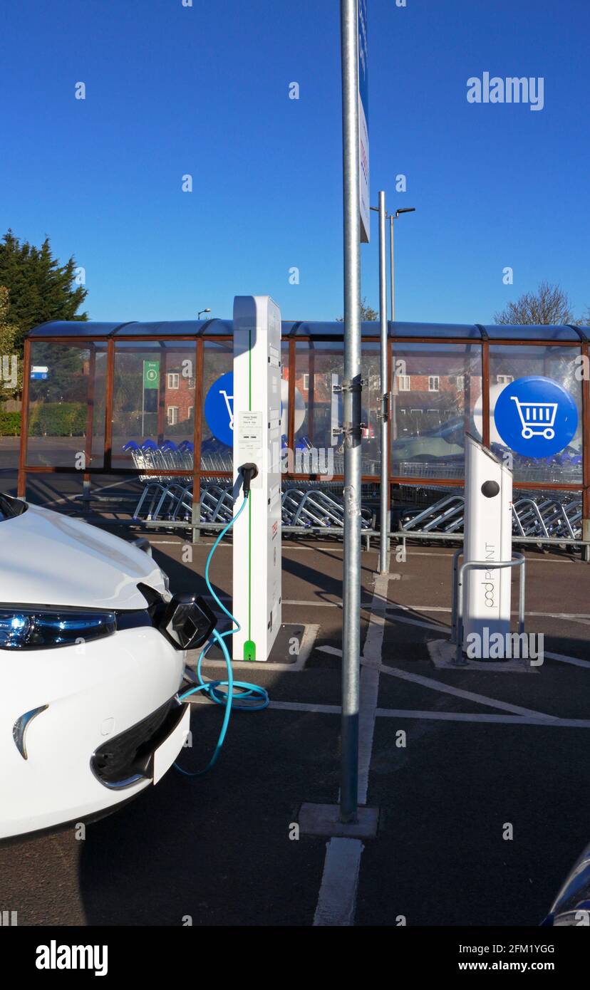 Ein Elektroauto, das mit einer Ladestelle in einem Supermarkt-Parkplatz in Sprowston, Norfolk, England, Großbritannien, verbunden ist. Stockfoto