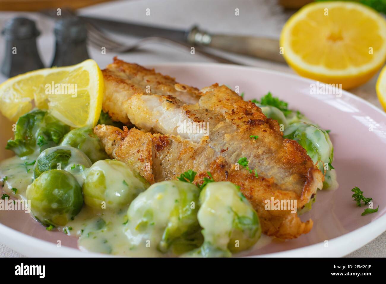 Gebratenes Fischfilet mit cremigen brüsseler Sprossen, serviert auf einem Teller auf Küchentisch Hintergrund Stockfoto