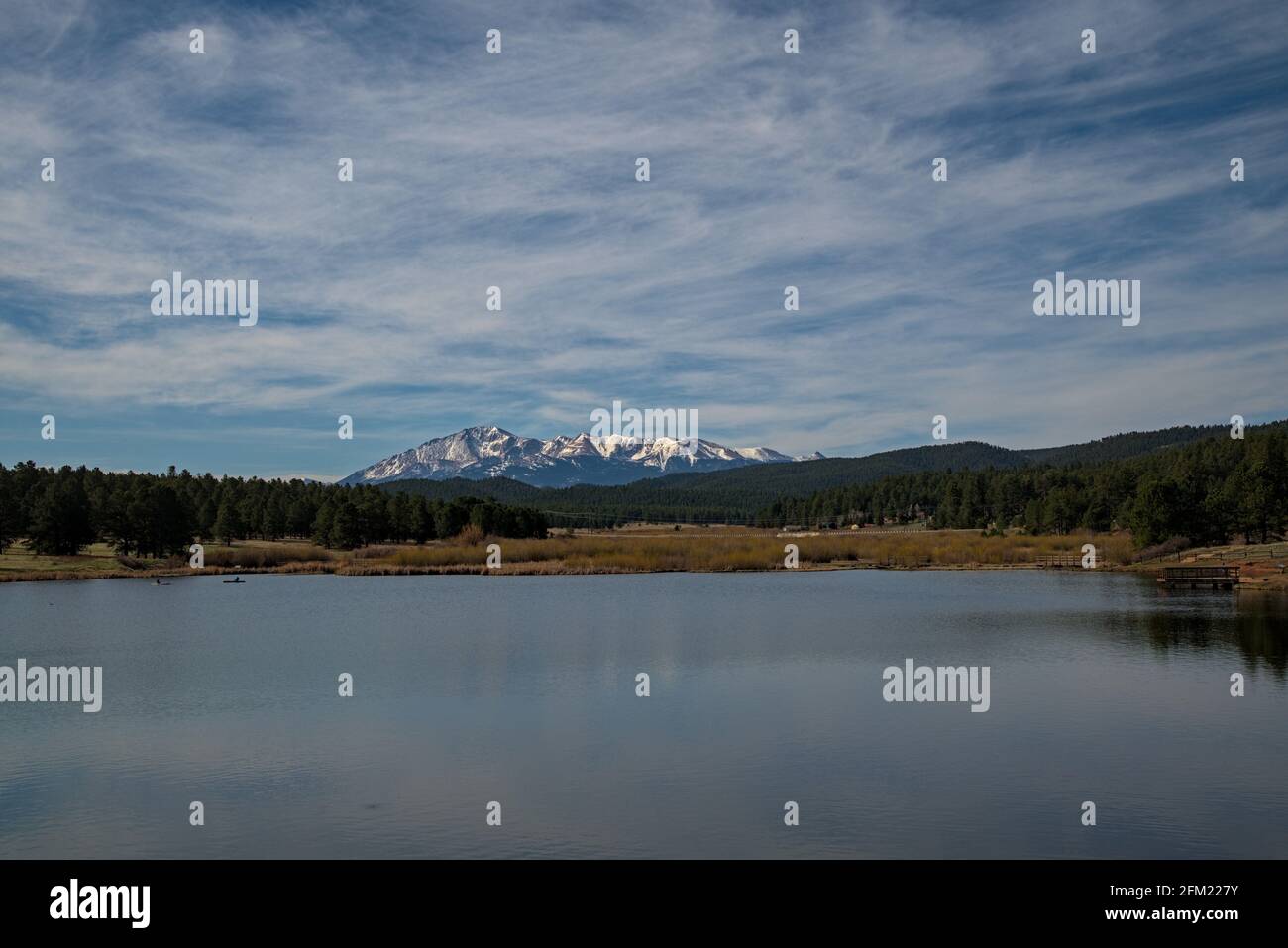 Manitou Lake an bewölktem Tag mit schneebedeckten Berghechten Spitze im Hintergrund eingerahmt von Flecken von feuchtenden Bäumen, wo die Menschen angeln Boot und wandern. Stockfoto