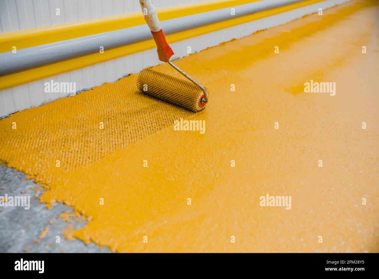 Arbeiter, der Epoxy- und Polyurethan-Fußbodensystem anwendet.Diese leicht zu reinigenden Produkte haben auch rutschfeste Eigenschaften. Stockfoto