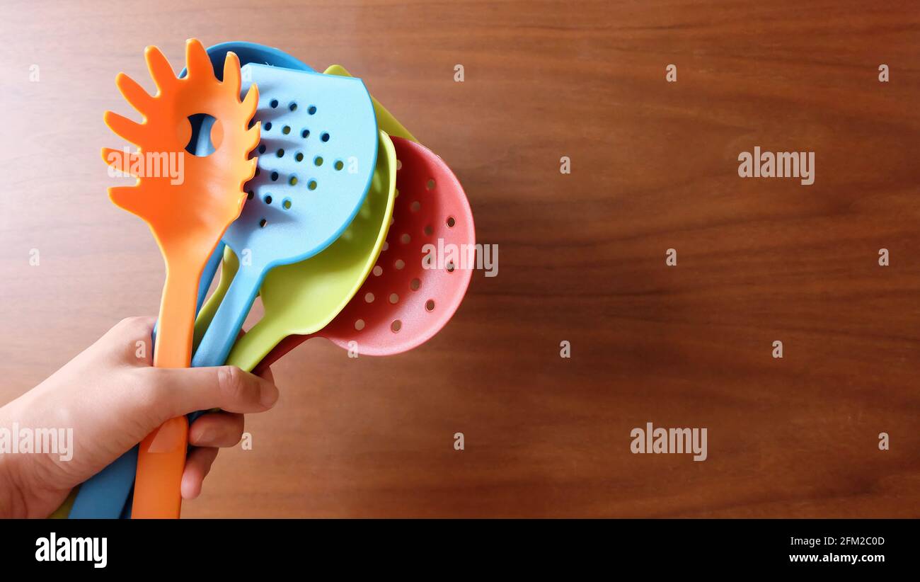 Eine Hand mit einer Vielzahl von farbenfrohen Kochutensilien und einem Holzhintergrund. Stockfoto