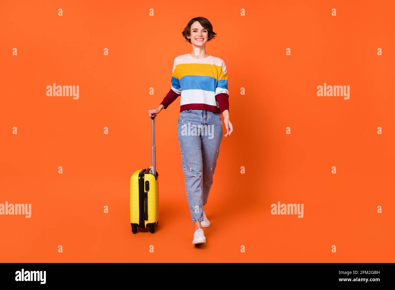 Foto in voller Größe von liebenswert zufrieden Mädchen zu Fuß tragen Tasche Toothy Lächeln isoliert auf orangefarbenem Hintergrund Stockfoto