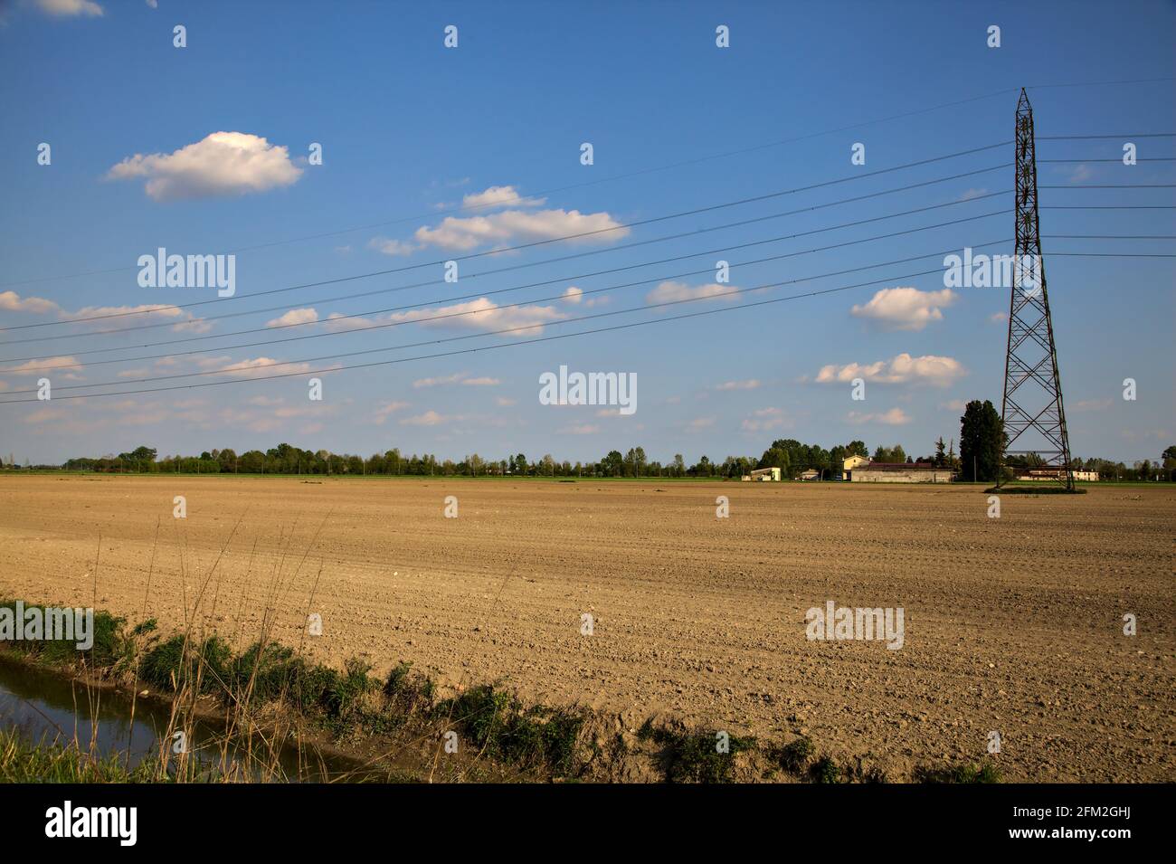 Gepflügte Feld mit einem Strompylon in der Mitte von Es an einem klaren Tag in der italienischen Landschaft Stockfoto