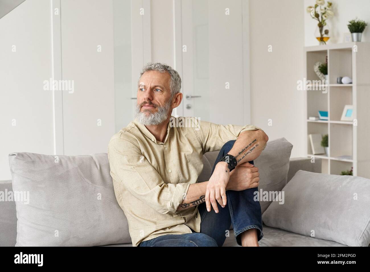 Entspannter reifer, nachdenklicher Mann, der auf dem Sofa sitzt und zu Hause denkt. Stockfoto