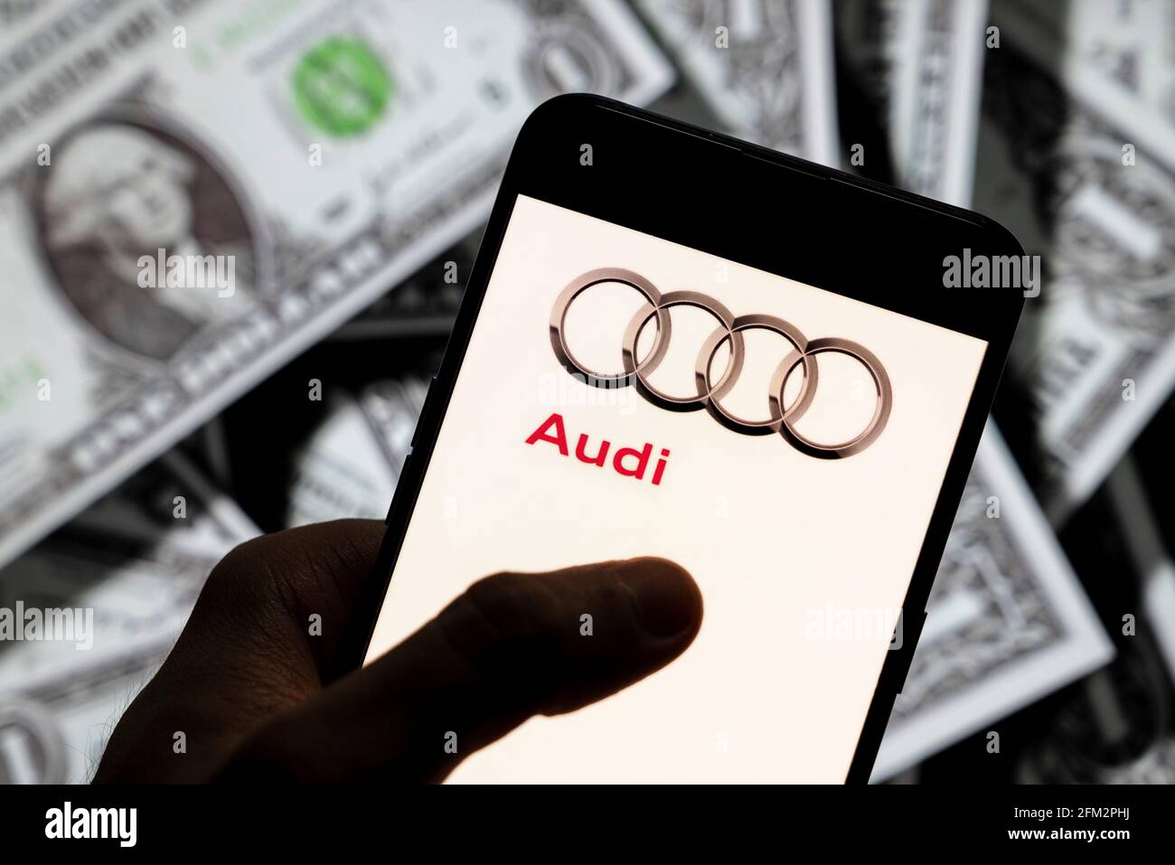 In dieser Abbildung ist das Logo des deutschen Automobilherstellers Audi zu sehen, das auf einem Smartphone mit US-Dollar-Währung im Hintergrund abgebildet ist. Stockfoto