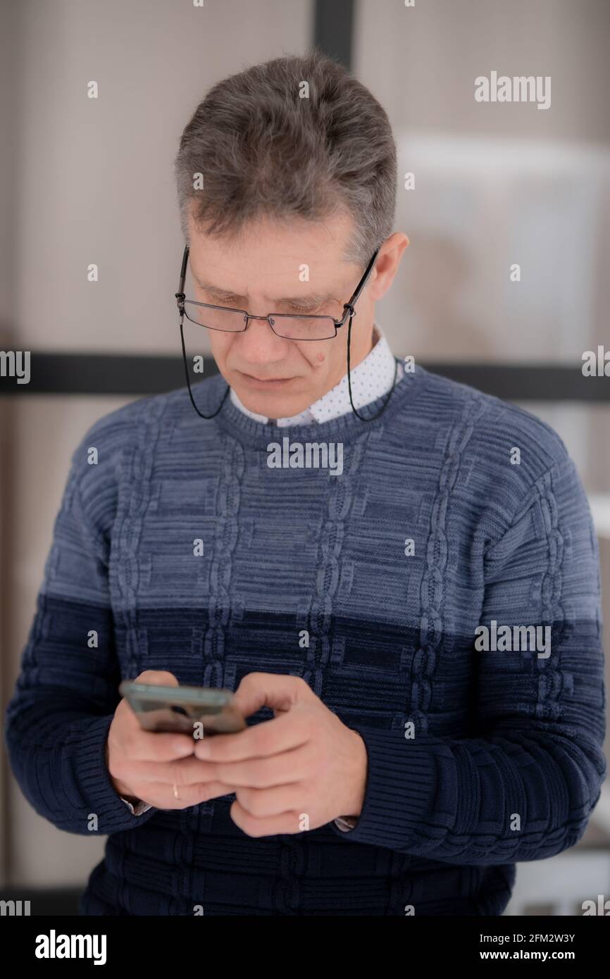 Ein grizzled Mann Geschäftsmann in einer Brille mit einem Telefon Vor dem Hintergrund eines Glasschirms Stockfoto