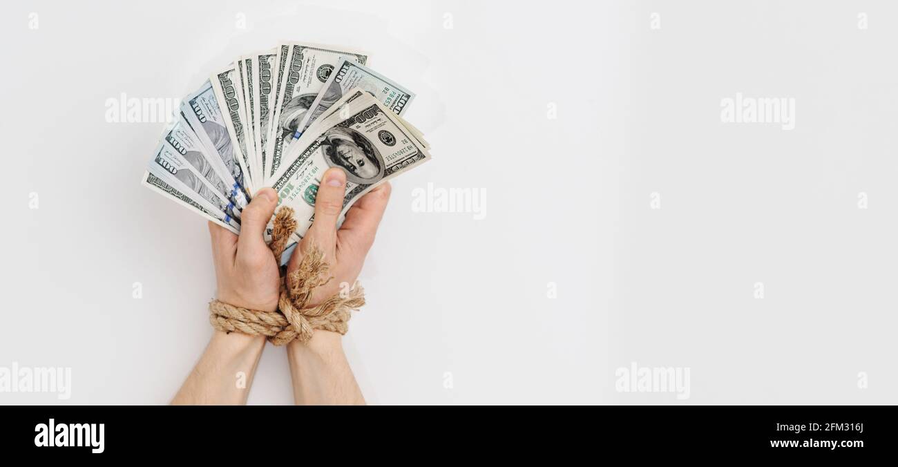 Ein Mann mit gefesselten Händen hält Dollar, Abhängigkeit von Geld, Rückzahlungen, Kreditrückstände Stockfoto