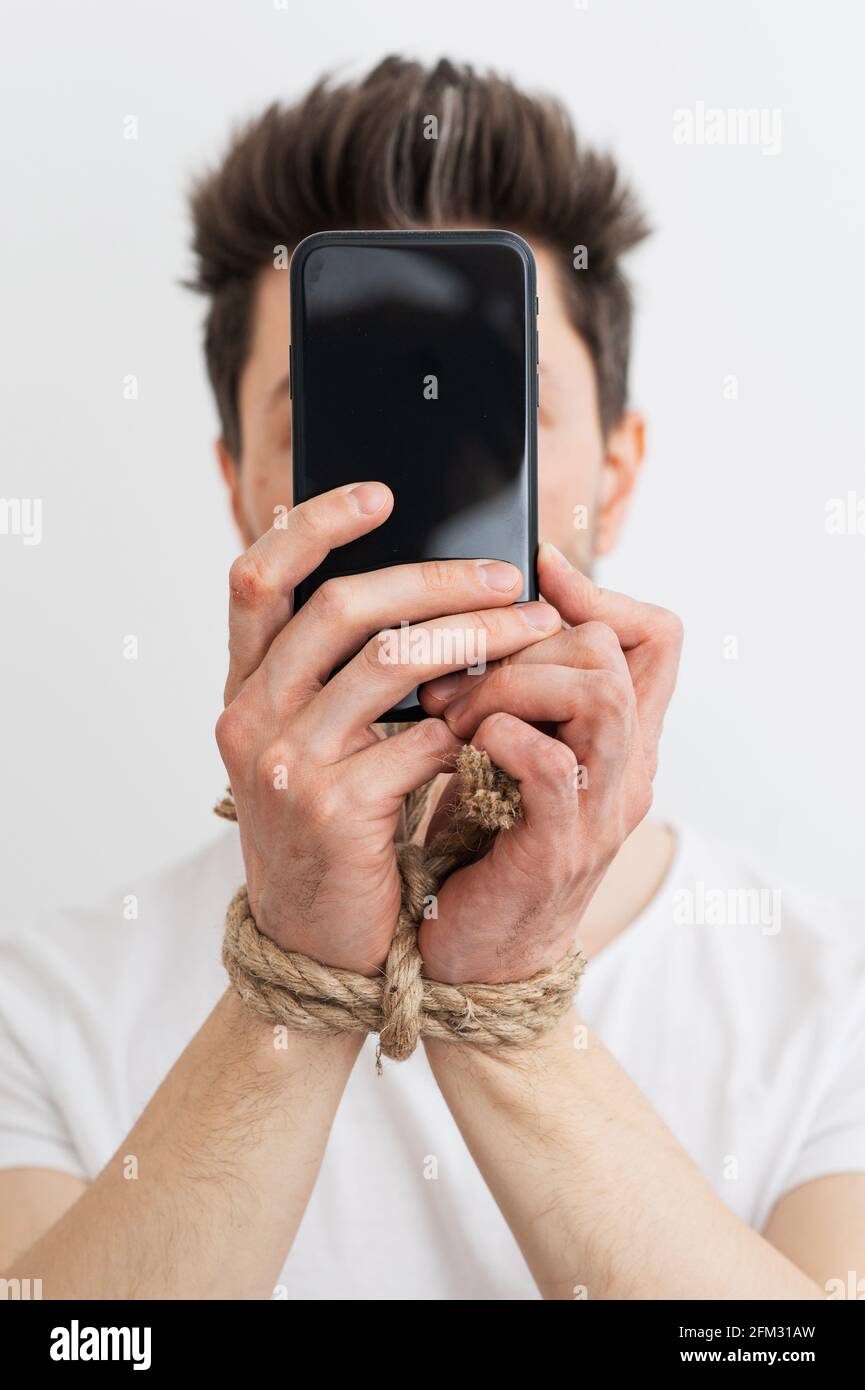 Eine Person mit gefesselten Händen, die ein Smartphone, eine Internetabhängigkeit oder eine sucht in sozialen Medien hält. Stockfoto