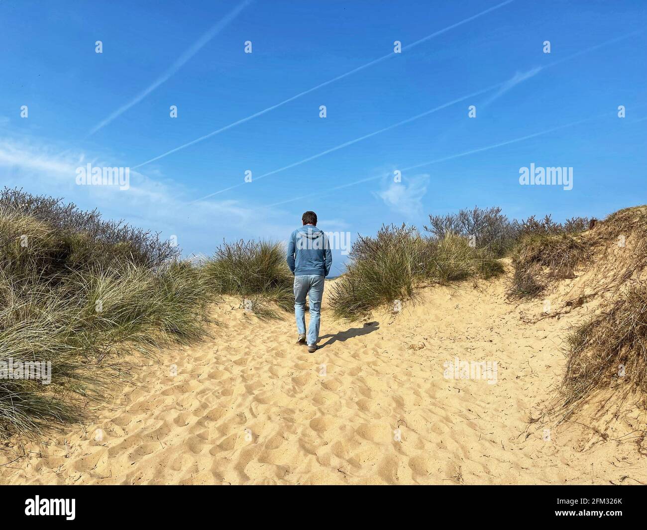 Rückansicht eines Mannes, der am Strand zwischen Sanddünen läuft, Norfolk, England, Großbritannien Stockfoto