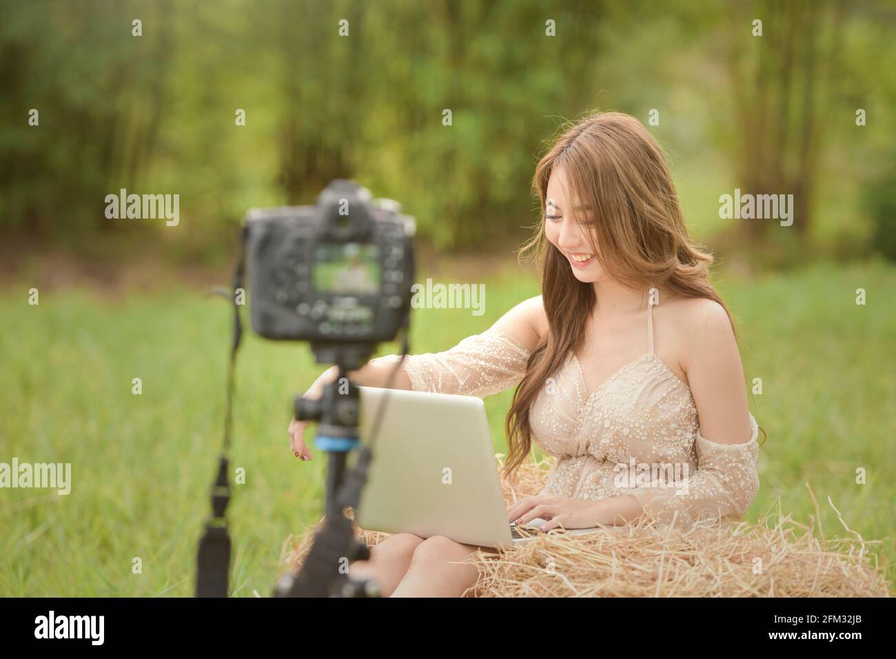 Schöne Frau, die auf einer Wiese sitzt und draußen filmt, Thailand Stockfoto