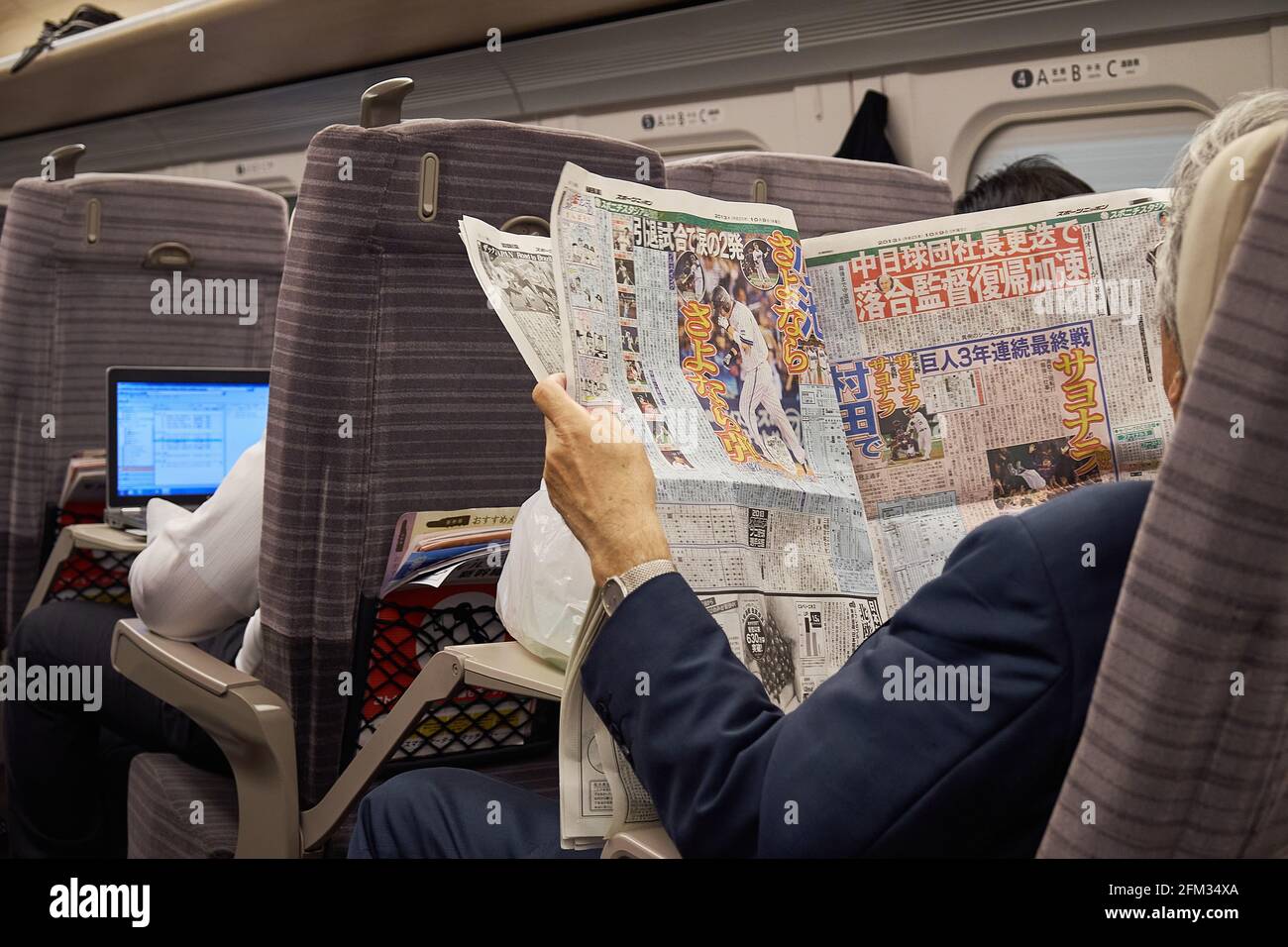 2 japanische Pendler auf einem Shinkansen-Hochgeschwindigkeitszug, eine Lesearbeit auf seinem Laptop und die andere, die eine Zeitung für Baseballsport liest, Japan Stockfoto
