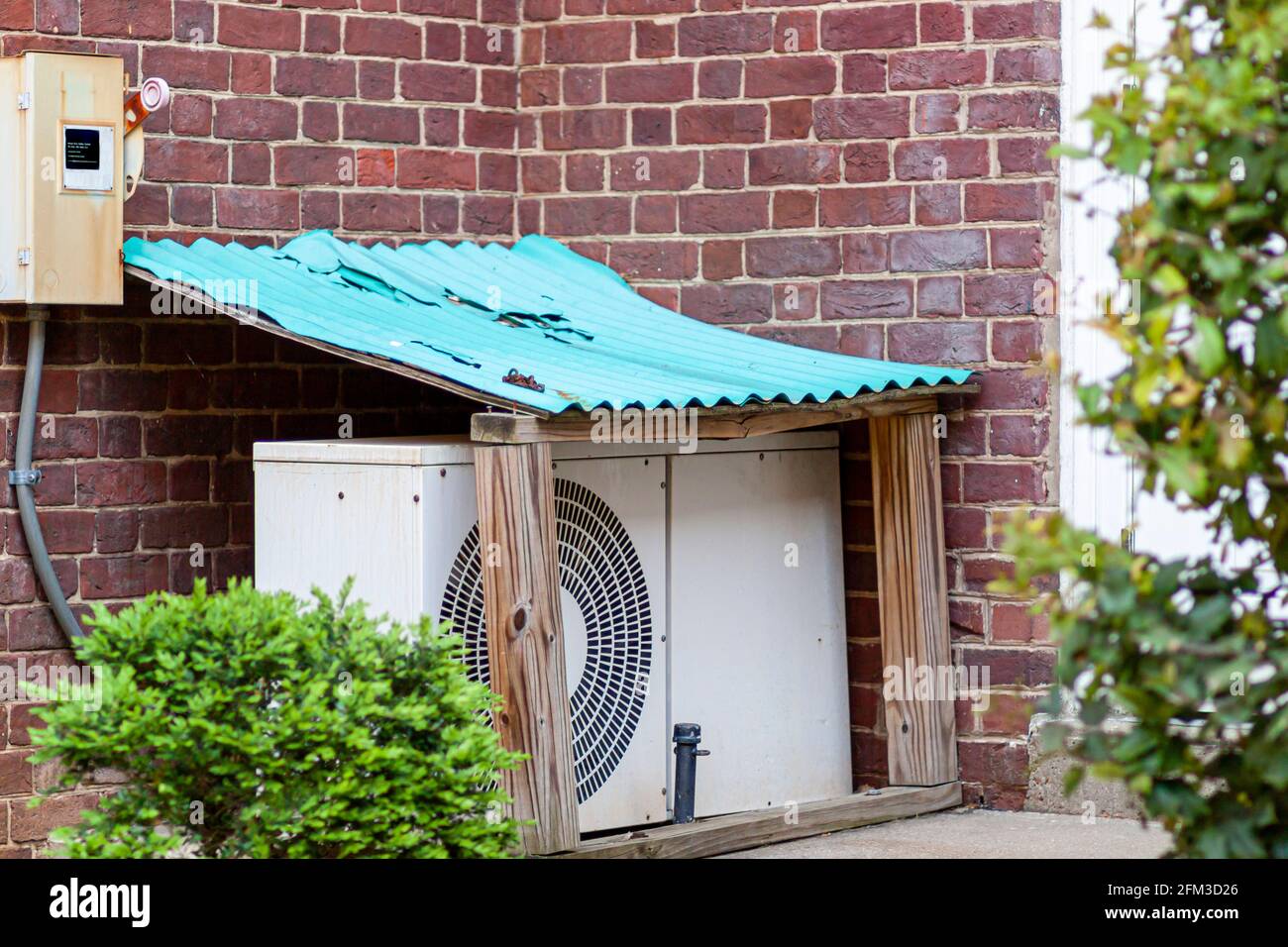 Eine Klimaanlage für den Außenbereich, die auf dem Boden in einem Garten in  einem kleinen Schutzschuppen mit lackiertem Wellblechdach aufgestellt wird.  Diese PR Stockfotografie - Alamy