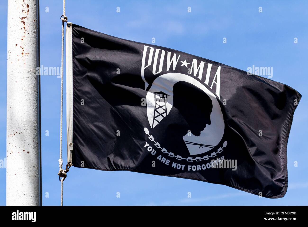 Nahaufnahme eines isolierten Bildes einer Kriegsgefangenen, MIA (Prisoner of war, Missed in Action) Flagge, die an einem sonnigen Tag im Wind fliegt. Emblem stellt die Silhouette eines Prisos dar Stockfoto