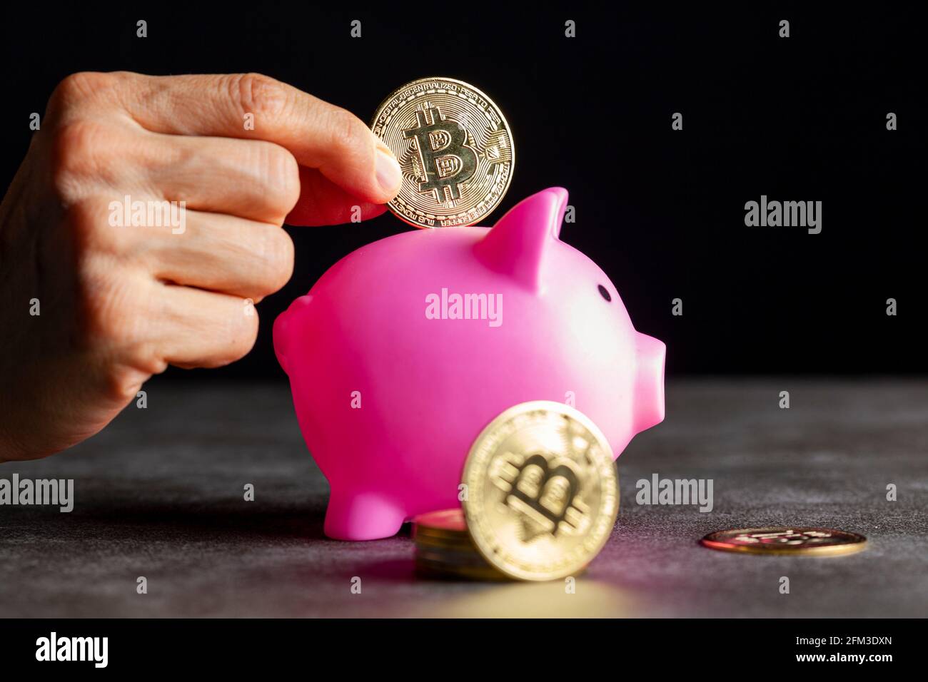 Konzeptbild für die Verwendung digitaler Krypto-Währung zur Ersparnis. Eine kaukasische Frau legt eine symbolische Bitcoin (BTC)-Münze in ein Sparschwein, um zu sparen Stockfoto