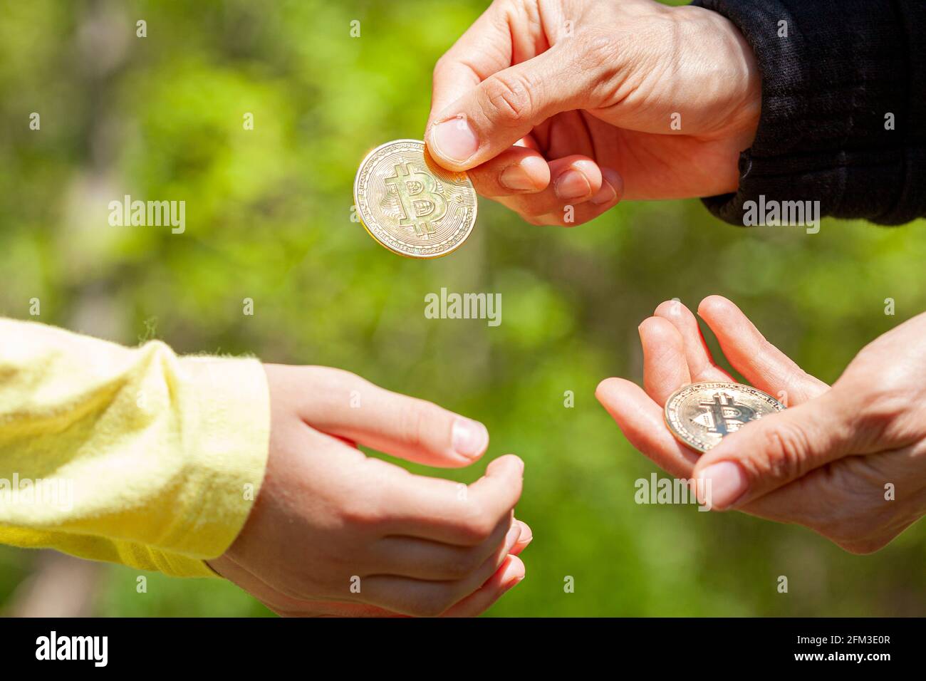 Ein Kind bittet um Taschengeld und seine Eltern geben als Antwort eine Bitcoin-Münze. Konzeptbild in Familieneinstellung zur Verwendung von Kryptowährung in d Stockfoto
