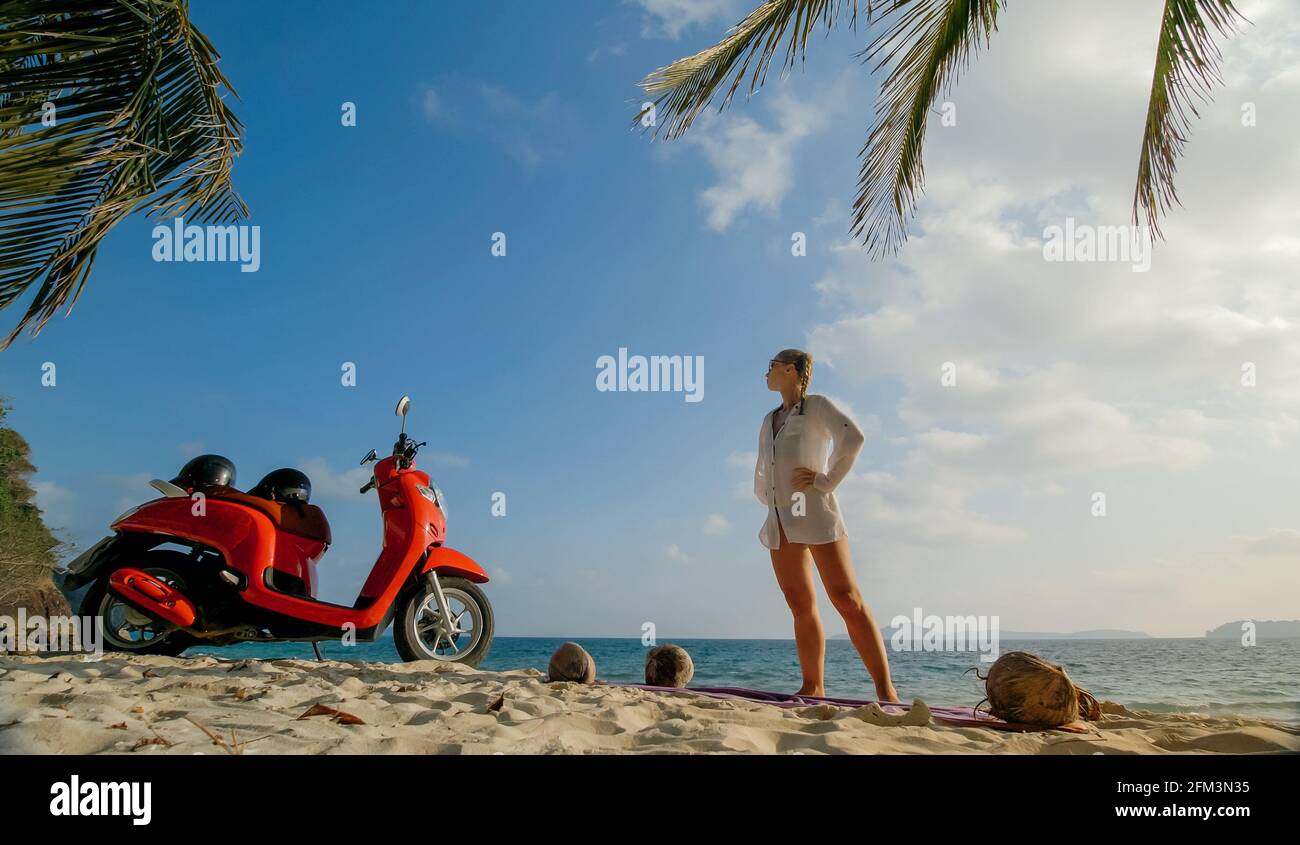 Motorroller Road Trip. Schönes Paar auf rotem Motorrad in weißen Kleidern am Sandstrand. Menschen, die in der Nähe der tropischen Palmen, Meer. Motorradmiete. Stockfoto